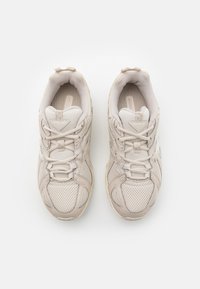 Chaussures de sport beiges avec dessus en maille, accents renforcés et semelle texturée. Comprennent un système de laçage et un col rembourré pour le confort.