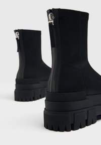 Stivaletti neri alla caviglia realizzati in materiale liscio, con suole spesse e seghettate e cerniere argentate sul retro per una facile vestibilità.