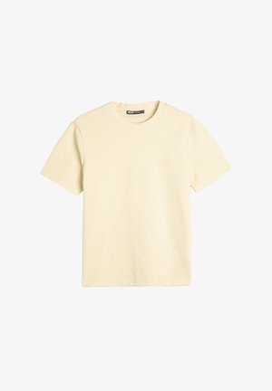 Camiseta de manga corta con cuello redondo en color beige claro, fabricada en un tejido texturizado con un patrón sutil, dobladillo recto y ajuste relajado. Sin logotipos ni gráficos visibles.