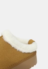 Scarpa slip-on in suede marrone con bordo in pelliccia bianca, collare arrotondato e suola in gomma testurizzata. Presenta dettagli di cucitura e un piccolo accento.