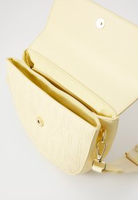 Borsa a tracolla in pelle gialla con texture, logo impresso, chiusura magnetica, hardware dorato e scomparti interni per l'organizzazione.