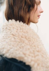 Collo in shearling beige su un capo esterno nero, che presenta una superficie morbida e strutturata con una forma arrotondata che cade sulla spalla.