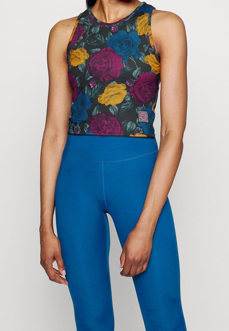 Květinový crop top s vícero barvami růží na tmavém pozadí, spárovaný s modrými legínami s vysokým pasem. Má kulatý výstřih a přiléhavý střih.