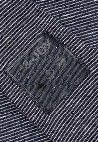 Gestreepte stof in navy en wit heeft een gestructureerd zwart etiket met een reliëflogo en tekst. Het materiaal lijkt geweven en duurzaam.