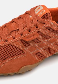 Orange suede sneaker with mesh panels, textured laces, and rubber outsole. Geox logo prominently displayed on the side and tongue.