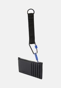 Carteira de pele preta com fecho de zíper, cinco slots para cartões, alça preta anexada e detalhe em hardware azul. Textura suave, design minimalista.