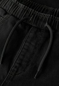 Los pantalones de chándal negros presentan una cinturilla elástica con cordón, una textura de tela suave y detalles de costura visibles en la zona de los bolsillos.