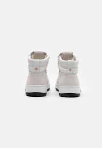Un paio di sneaker alte bianche e grigie chiare con suole nere viste di spalle su uno sfondo bianco.