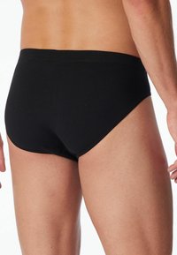 Schwarze Baumwollunterhose mit glatter Textur, körperbetontem Schnitt und niedriger Taille. Verfügt über einen flexiblen Bund und keine sichtbaren Marken oder Muster.