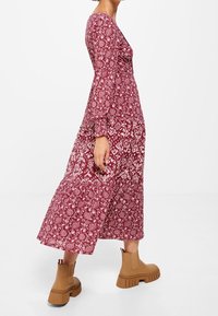 Vestido largo en color burdeos con un patrón floral y mangas largas; combinado con botas de tobillo en color beige; tejido fluido con un dobladillo en capas.