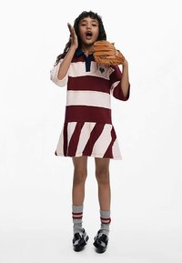 Rochie cu dungi în culorile bordo și crem, cu guler polo și fustă evazată. Accesoriile includ o mănușă de baseball maro și șosete gri.