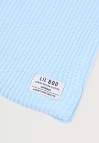 Sciarpa a coste azzurro chiaro con un'etichetta tessuta che riporta "LIL'BOO," e il testo "DANISH DESIGN STUDIOS COPENHAGEN," e "KEEPING IT HYGGE SINCE 2016."