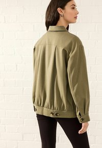 Olivgrüne Jacke mit entspannter Passform, ausgestattet mit einem Reverskragen, Knopfakzenten an den Ärmeln und einem gerafften Saumdetails.