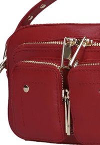 Rode crossbody tas met een gestructureerd oppervlak, dubbele ritssluitingen, goudkleurige hardware en een schouderband met studs.