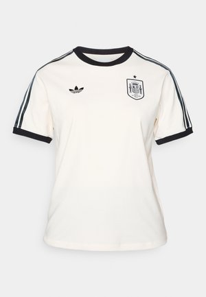 Camiseta color crema con cuello y puños negros, que presenta el logotipo negro de Adidas y el escudo de la selección nacional de España, además de rayas oscuras en las mangas.