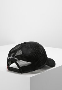 Gorra negra con una parte frontal sólida y parte trasera de malla, con visera curvada. Detalle notable: texto bordado en blanco en la parte posterior. Correa ajustable.
