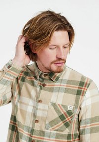 Miesten flanellipaita, jossa on beige, vihreä ja oranssi ruutukuosi. Paita on nappikiinnityksellä edessä ja siinä on rintatasku, jossa on logotägi.