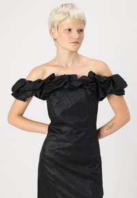 Μαύρο φόρεμα με έναν ώμο, με ρίγες στον γιακά, φτιαγμένο από υφασμάτινο υλικό με γυαλιστερή υφή. Κοντό προς το μέσο μήκος, εφαρμοστό σχήμα, με ομαλή σιλουέτα.
