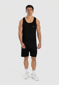 Zwarte tanktop en korte broek set van lichtgewicht stof. Witte logo-detail op de top en korte broek. Accessoires zijn witte sneakers en sokken.