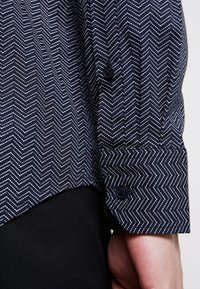 Námořnická modrá košile na knoflíky s bílým cikcak vzorem, má detailem na manžetách a černý knoflík, vyrobena z prodyšné látky.