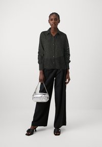 Σκοτεινό πράσινο πουκάμισο με δαντελένια μανίκια, συνδυασμένο με μαύρους παντελόνες ψηλής μέσης και ασημένια τσάντα με αλυσίδα. 