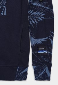 Manica di felpa blu navy con stampe di foglie tropicali azzurro e patch con logo O'Neill che presenta onde in tonalità blu.