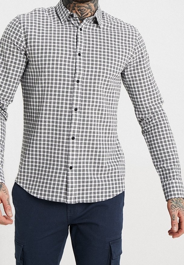 Geverifieerde button-up blouse in zwart-wit, lange mouwen, slim fit, met kraag en zwarte knopen tegen een ruitpatroon.