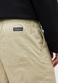 Μπεζ σορτς Patagonia με ελαστική μέση και πίσω τσέπη, φορεμένα με μαύρο μακρυμάνικο τοπ, εμφανίζοντας μέρος του δεξιού χεριού.