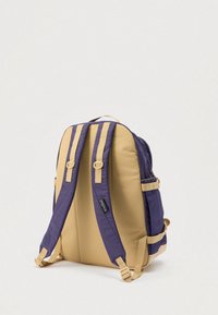 Σακίδιο πλάτης με χρωματικό συνδυασμό μωβ και μπεζ, με επενδυμένο σώμα, ρυθμιζόμενους ιμάντες και πολλαπλές εξωτερικές τσέπες. Ομαλή υφή.