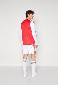 Rød atletisk trøje med hvide ærmer, tekstureret ryg, parret med hvide shorts med røde detaljer og sokker med sorte striber.