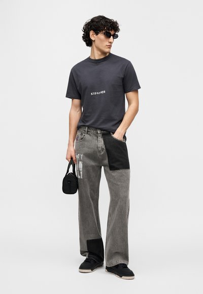 Γκρι μπλουζάκι με στάμπα «KID SUPER», σε συνδυασμό με φαρδιά τζιν παντελόνια σε μαύρο και γκρι με εύκολες ραφές. Μαύρα γυαλιά ηλίου και μικρό τσαντάκι ολοκληρώνουν την εμφάνιση.