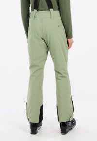 Pantalons de ski verts avec des accents noirs, bretelles réglables et larges ouvertures aux jambes. Fabriqués à partir d'un matériau imperméable, conçus pour les sports d'hiver.
