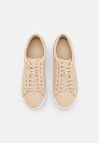 Beige leather sneakers with a textured finish, rounded toe, white rubber sole, and flat laces. Gold accents near the heel.
