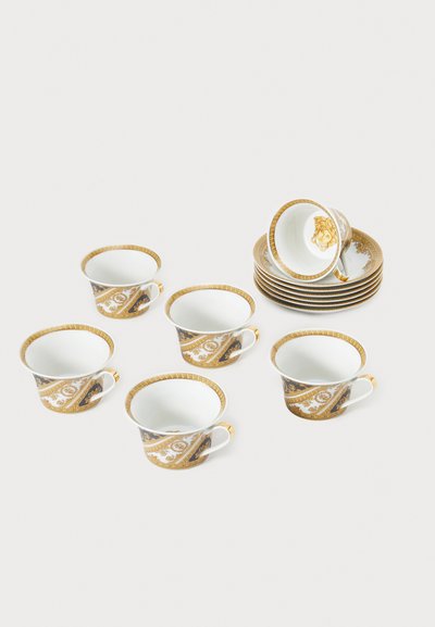 Kuusi posliinikuppia, joissa kullatut ja mustat koristekuviot, kaarevat kahvat ja kiiltävä pinta. Taustalla pinotut lautaset.