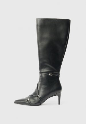 Bota de cuero negra hasta la rodilla con punta afilada, tacón fino y correas decorativas con pequeñas hebillas.