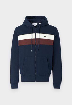 Marineblå hettegenser med hvite og burgunder horisontale striper, kenguru-lommer, snorhette og Lacoste-logo på brystet.