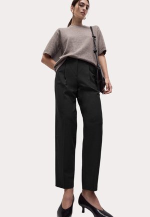Pull court beige à manches courtes associé à un pantalon noir taille haute et des escarpins noirs ; design simple avec une coupe ajustée.