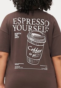 Brūns T-krekls ar kafijas krūzes grafiku, kurā izceltas frāzes "Izpaud sevi ar espresso" un "Kafija līdzi!!!"