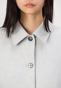 Ανοιχτό γκρι, υφασμάτινο πουκαμίσα με υφή που διαθέτει μεγάλο γιακά και δύο στρογγυλά κουμπιά μπροστά, σχεδιασμένο με απαλή, υφαντή ύφασμα.