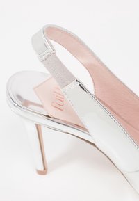 Talons slingback en cuir verni argenté avec une semelle intérieure rembourrée rose, présentant une silhouette élancée et une finition lisse et brillante.