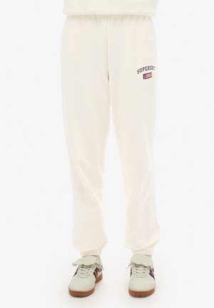 Crème kleurige joggingbroek met elastische boorden, voorzien van het "Superdry" logo en vlag borduursel op de linker dij. Gestructureerde stof.