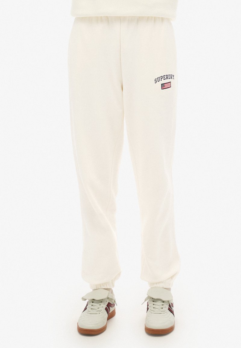 Crème kleurige joggingbroek met elastische boorden, voorzien van het "Superdry" logo en vlag borduursel op de linker dij. Gestructureerde stof.