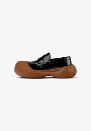 Chaussure noire en cuir à enfiler avec un bout arrondi, dotée d'une semelle en bois texturé tan et d'une sangle décorative sur le dessus.