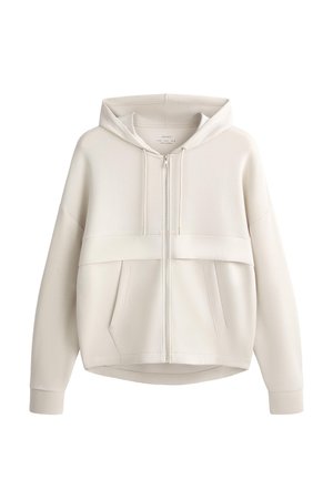 Jasnobeżowa bluza z kapturem na zamek, z suwakiem z przodu, kapturem ze sznurkiem, długimi rękawami oraz dwoma przednimi kieszeniami widocznymi na białym tle.