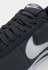 Černé kožené tenisky s tmavě šedým šněrovacím designem. Obsahují bílé logo Nike swoosh a texturované detaily na svršku.