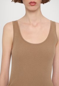 Ribbed, ilman hihoja oleva toppi vaaleanruskeana, jossa on pyöreä pääntie ja kapea design. Pehmeä rakenne näkyy.