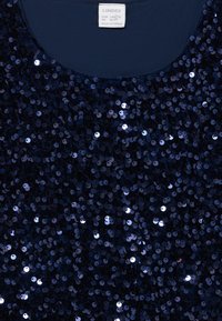 Marineblå top dækket af pailletter, med rund halsudskæring og glat stofbase. Etiketter er synlige øverst.