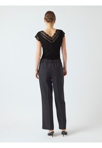 Zwarte top met kantafwerking op een V-vormige rug, gecombineerd met hoogwaardig, losvallende donkere broeken. Model draagt zwarte hakken.