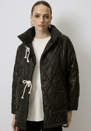 Veste noire matelassée avec un col haut, dotée de cordons et de boutons crème. Texture lisse, tissu léger et coupe oversize.