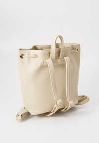 Sac seau beige en simili cuir lisse. Équipé de quincaillerie dorée, de bretelles ajustables et de deux poignées supérieures. Forme arrondie.